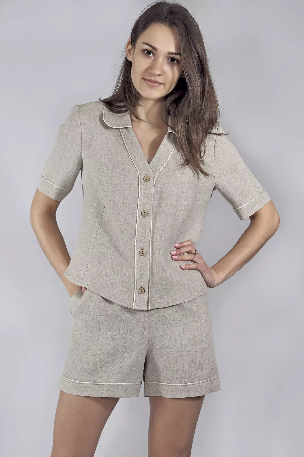Modelka stoi prosto, opierając jedną rękę na biodrze. Prezentuje przód koszuli piżamowej Kinia. Widać detale: naturalne, brązowe guziki oraz precyzyjnie wszytą jasną wypustkę, która podkreśla linię zapięcia i kołnierzyka.