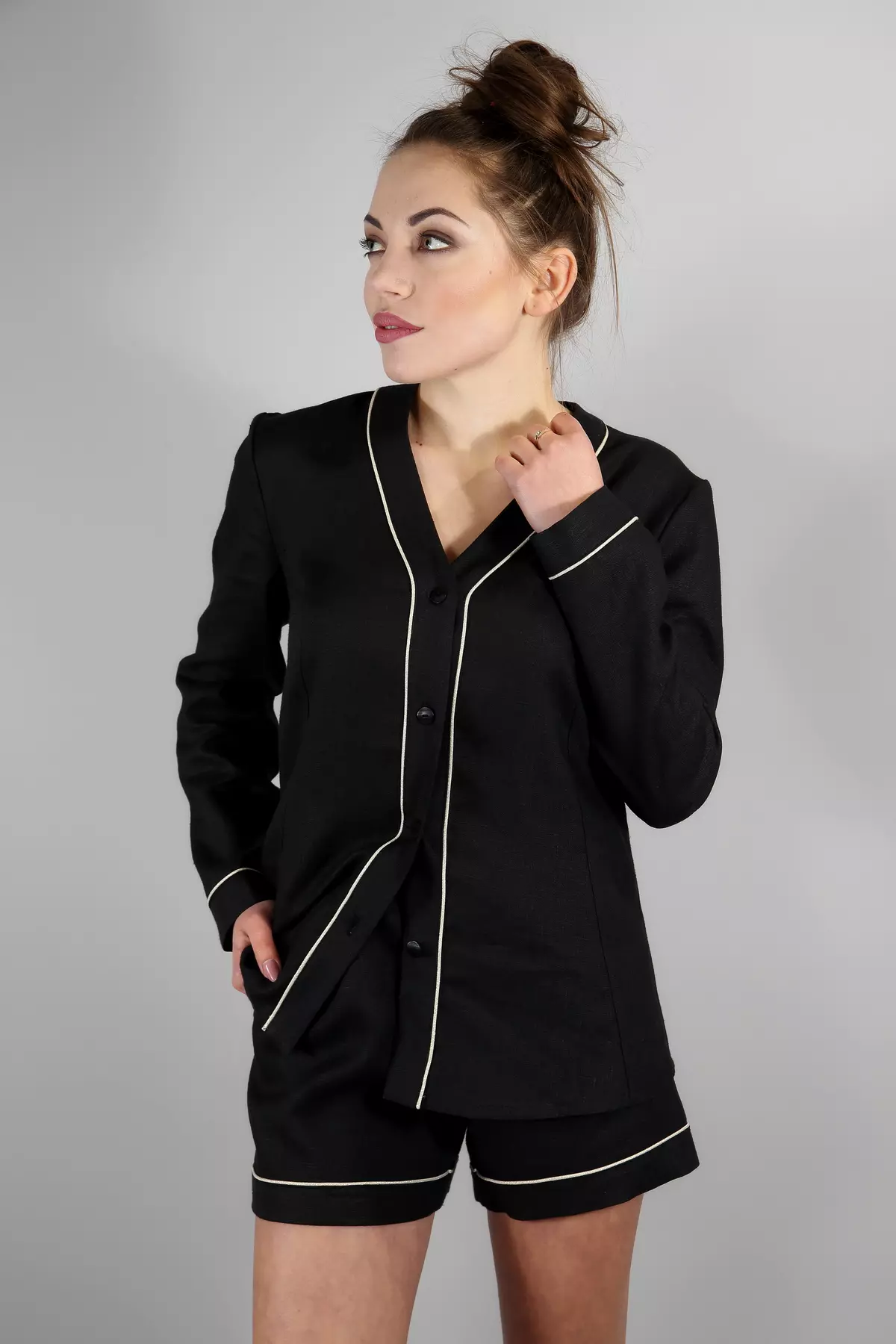 Modelka stoi w półprofilu, dotykając dłonią szyi. Ma na sobie czarną, lnianą koszulę Daga z długim rękawem i dekoltem w serek (bez kołnierzyka). Do kompletu dobrała krótkie szorty. Jasna wypustka przy krawędziach pięknie kontrastuje z czernią.