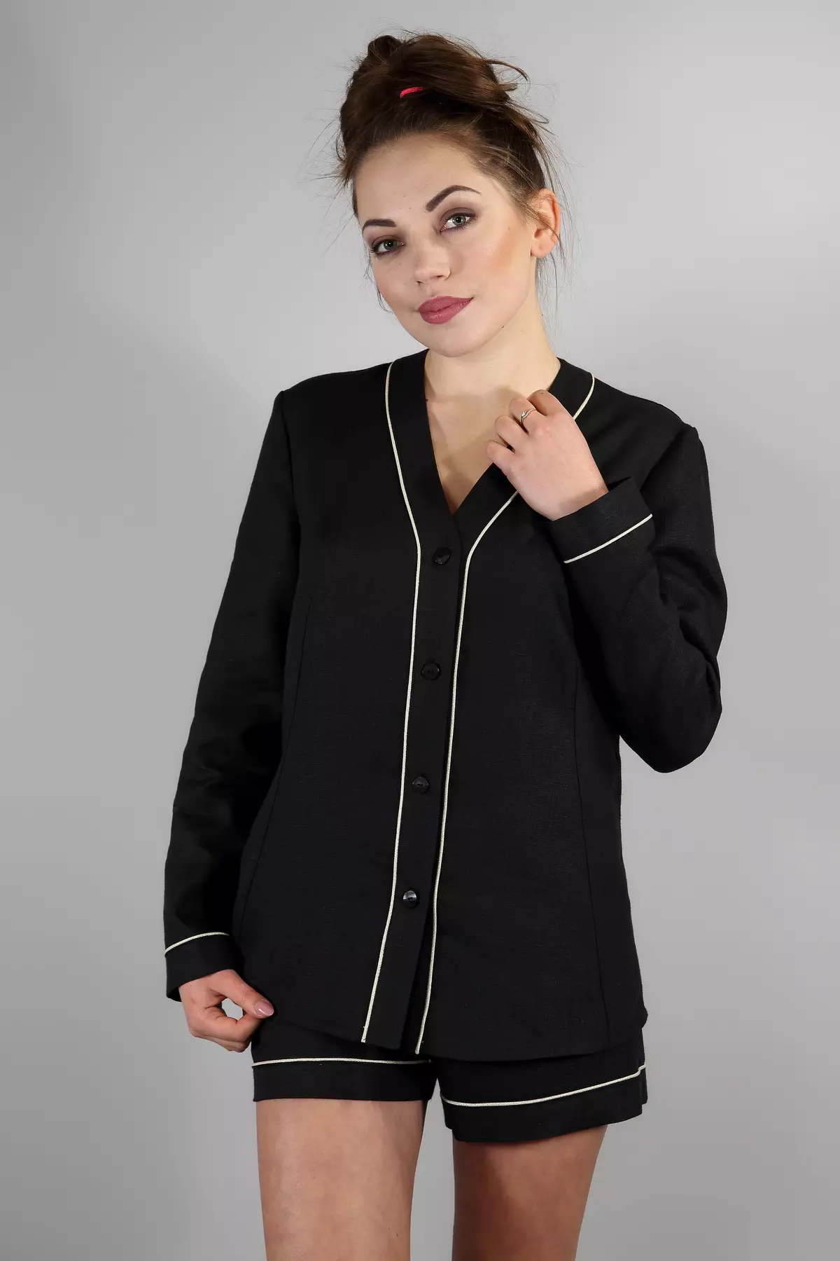 Uśmiechnięta brunetka trzyma rękę na głowie. Prezentuje czarny zestaw Daga: koszulę z długim rękawem i szorty. Luźny krój i miękki len zapewniają wygodę. Widać staranne wykończenie jasną wypustką.