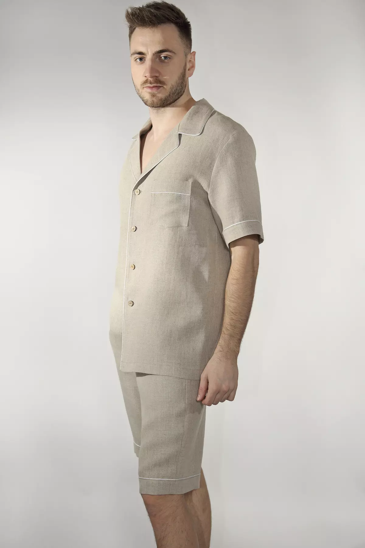 Mężczyzna w półprofilu. Prezentuje górną część piżamy Remi. Widać surową fakturę niebarwionego lnu i naturalne guziki. Krótki rękaw zapewnia swobodę. Koszula ma luźny, komfortowy krój.
