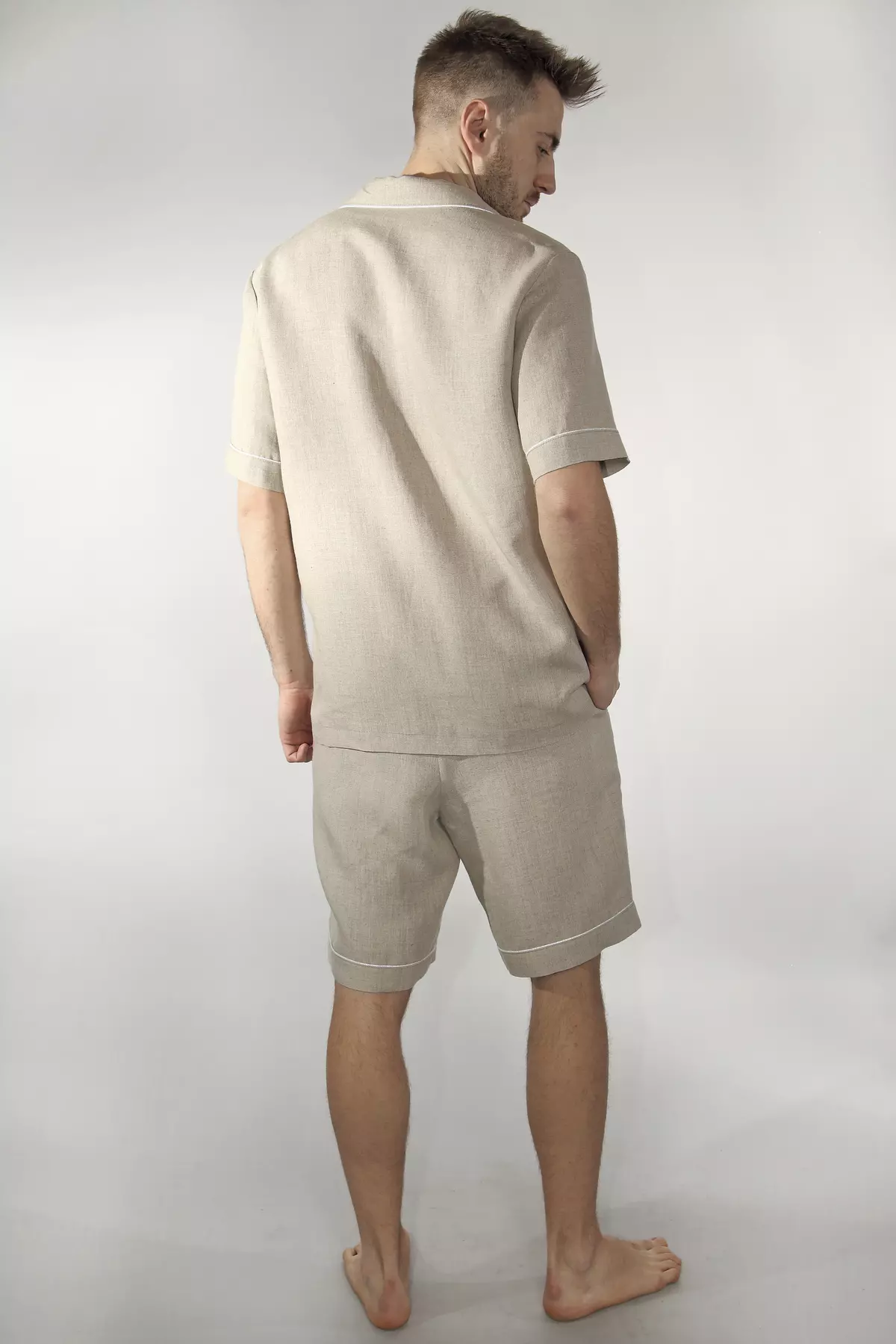 Widok pleców mężczyzny. Koszula Remi ma prosty tył z karczkiem. Krótkie rękawy i nogawki szortów są wykończone jasną lamówką. Widać, jak naturalny len miękko układa się na sylwetce.
