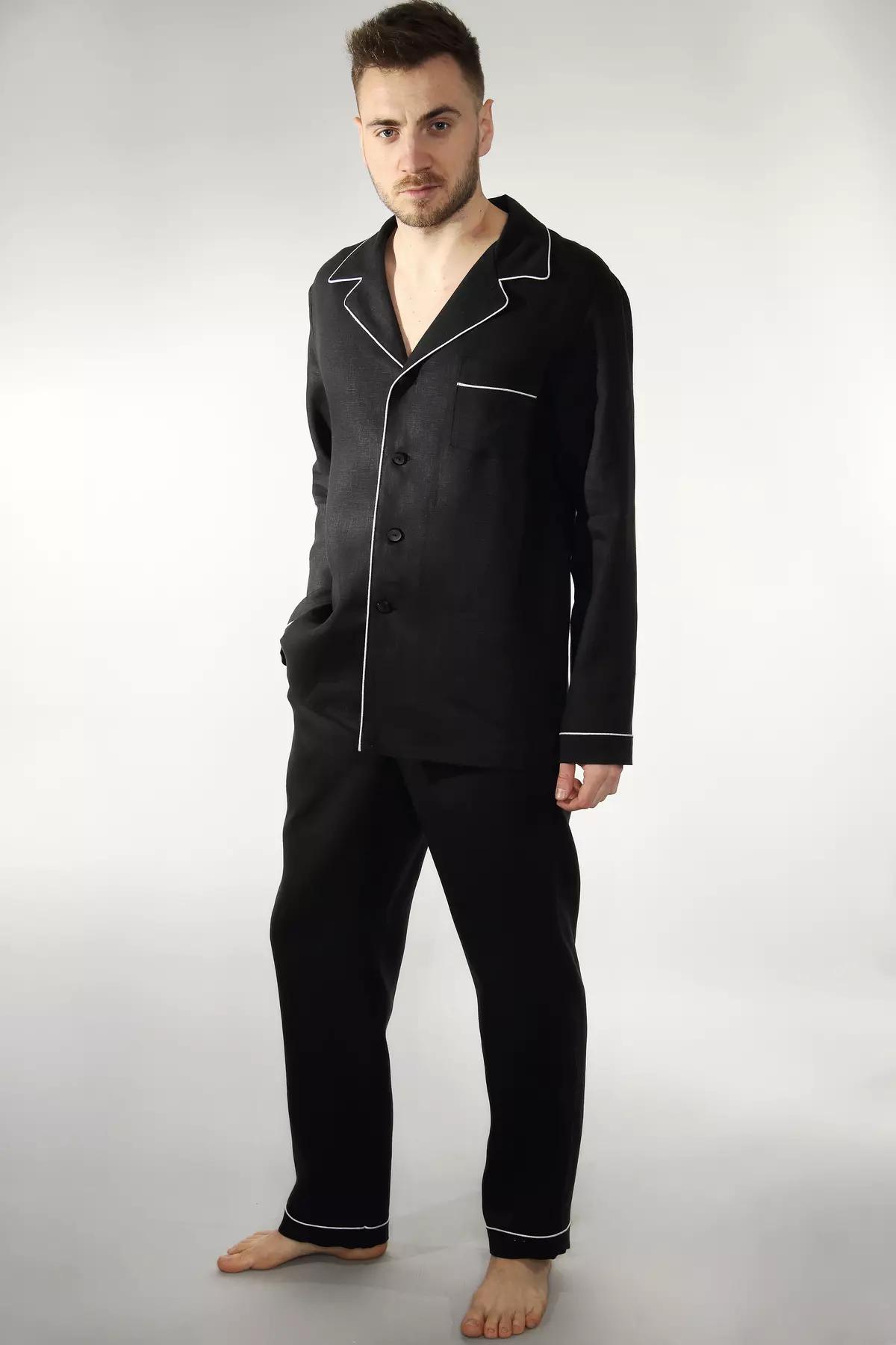Mężczyzna stoi w lekkim rozkroku, patrząc w obiektyw. Ma na sobie czarną piżamę z długimi spodniami. Luźny krój zapewnia wygodę, a czarny kolor dodaje klasy. Idealny strój na chłodniejsze noce lub leniwy dzień w domu.