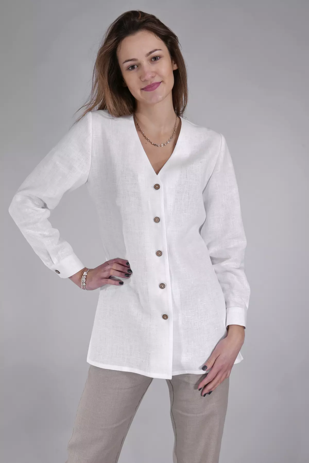 Modelka w półprofilu, z jedną ręką na biodrze. Bluzka ma luźny, wygodny fason tuniki. Widać boczne rozcięcia na dole, które zapewniają swobodę ruchów. Biały len wygląda elegancko i świeżo.
