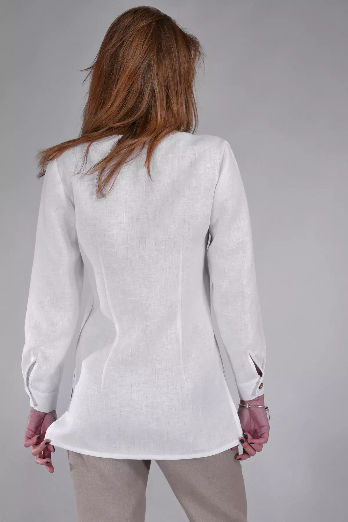 Widok pleców modelki. Bluzka Lara ma prosty, dłuższy krój zakrywający biodra. Widać pionowe przeszycia (zaszewki) modelujące sylwetkę. Długie rękawy zakończone są mankietami.