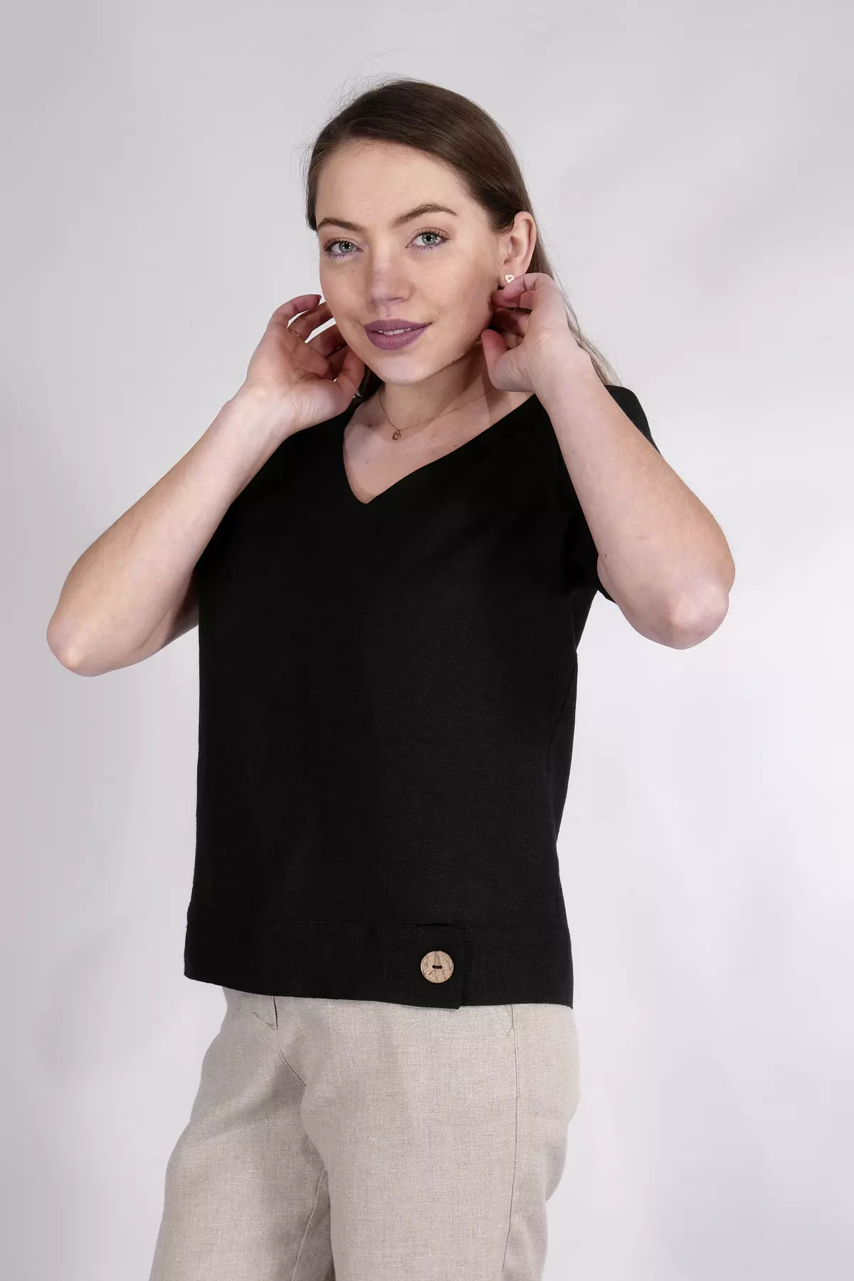 Zbliżenie na górną część sylwetki. Modelka poprawia włosy, eksponując dekolt w serek (V-neck). Widać fakturę czarnego lnu oraz złoty naszyjnik. Bluzka ma prosty, luźny krój ramion.