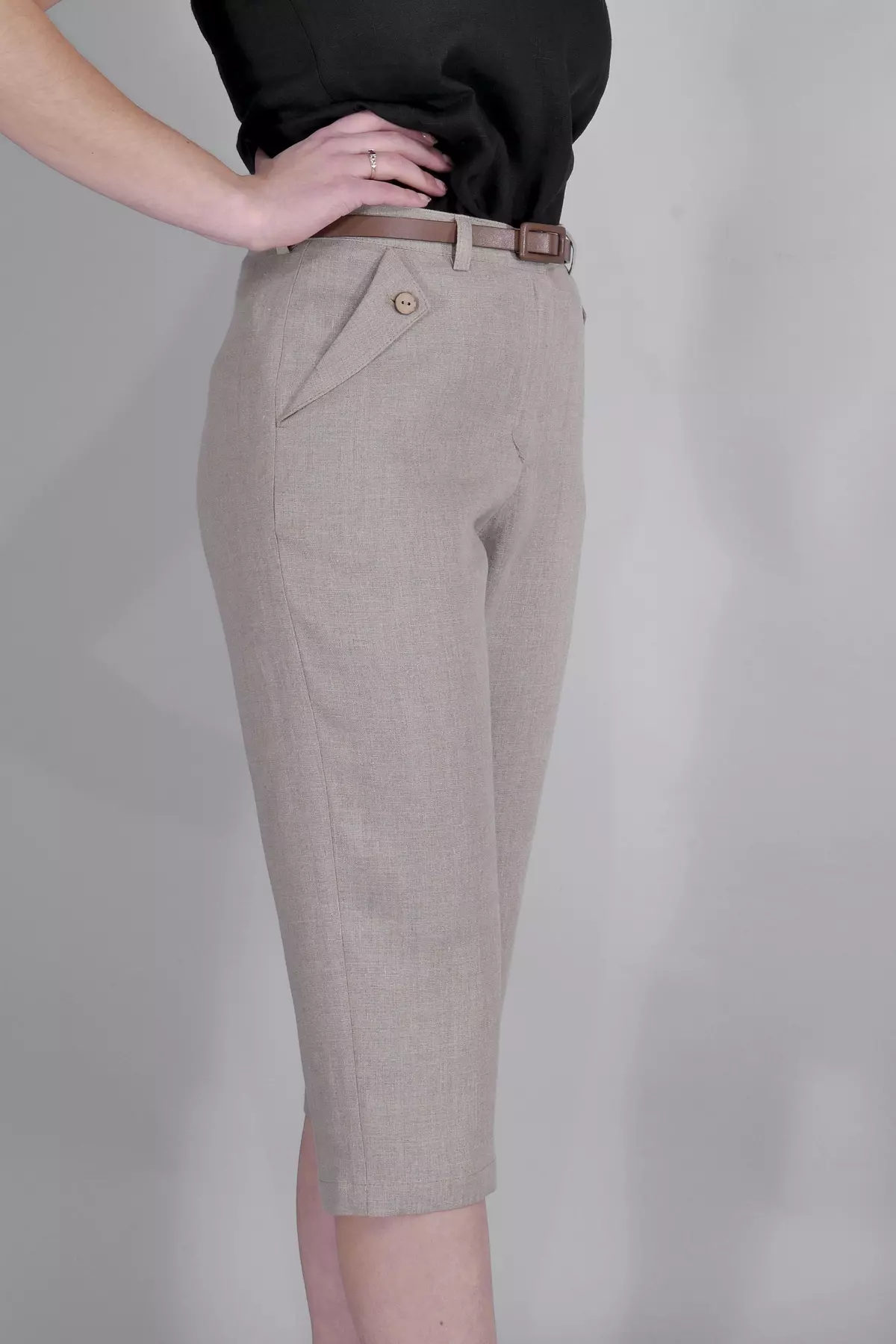 Modelka stoi bokiem. Ręce opiera na biodrach.Ujęcie pokazuje, jak naturalny len układa się na biodrach i udach. Spodnie są lekko dopasowane, ale nie obcisłe.