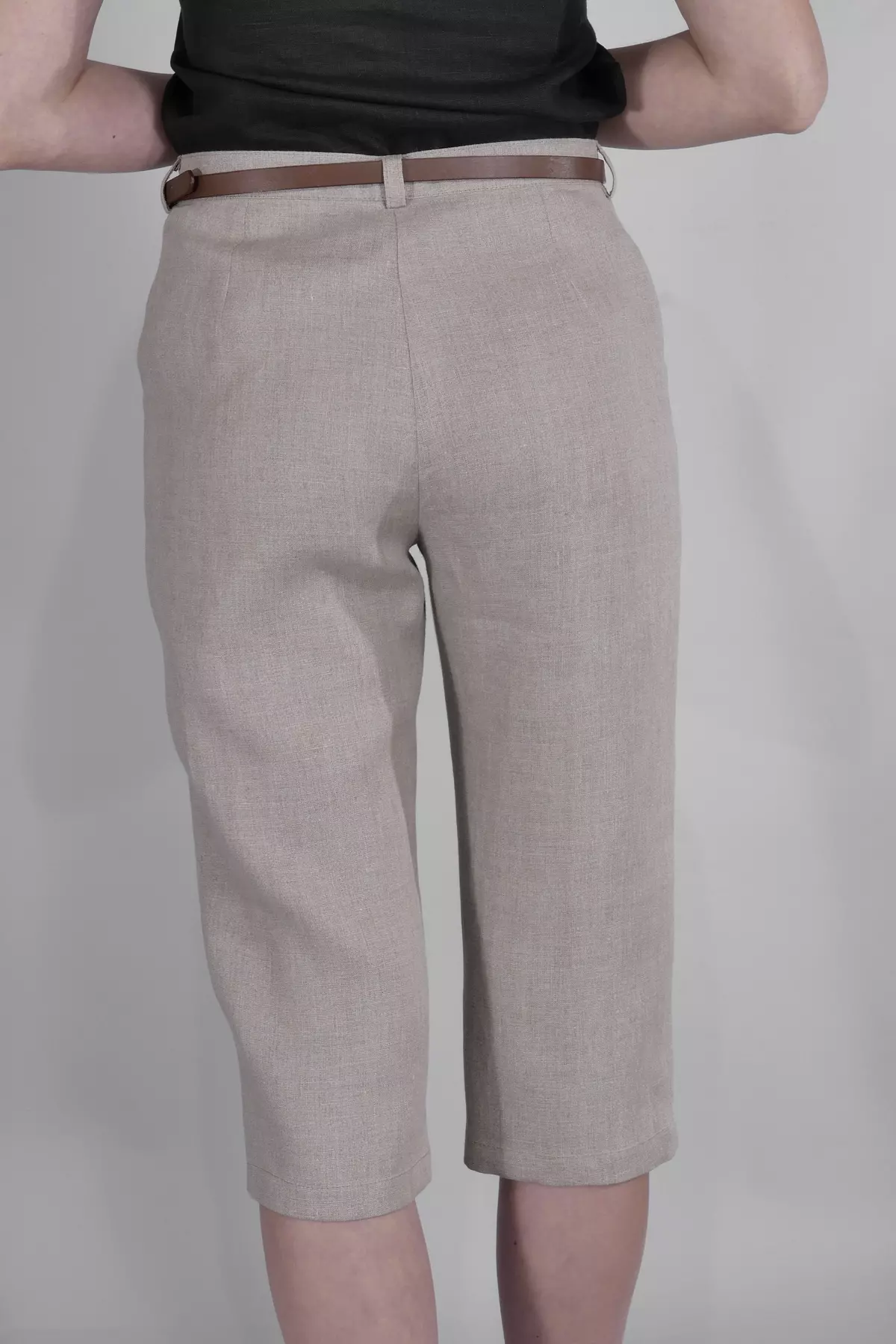 Widok spodni od tyłu. Nogawki Nata są proste i kończą się za kolanem. Widać fakturę niebarwionego lnu i brązowy pasek w szlufkach. Góra stylizacji to czarny top.