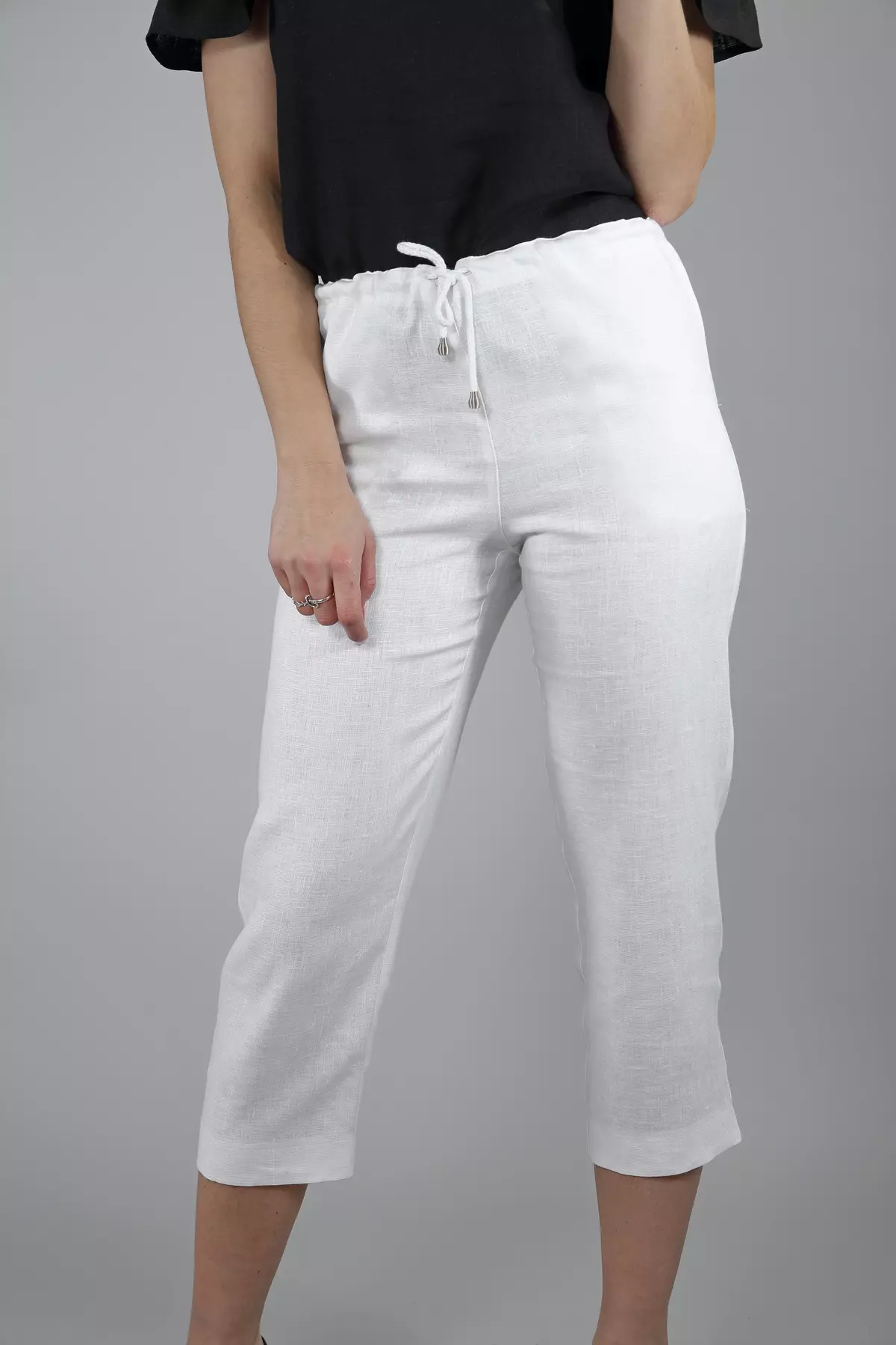 Zbliżenie na górną część spodni. Modelka trzyma rękę w kieszeni. Wyraźnie widać elastyczną gumkę w talii oraz biały sznurek ze srebrnymi końcówkami, służący do regulacji. Materiał ma widoczny splot lnu.