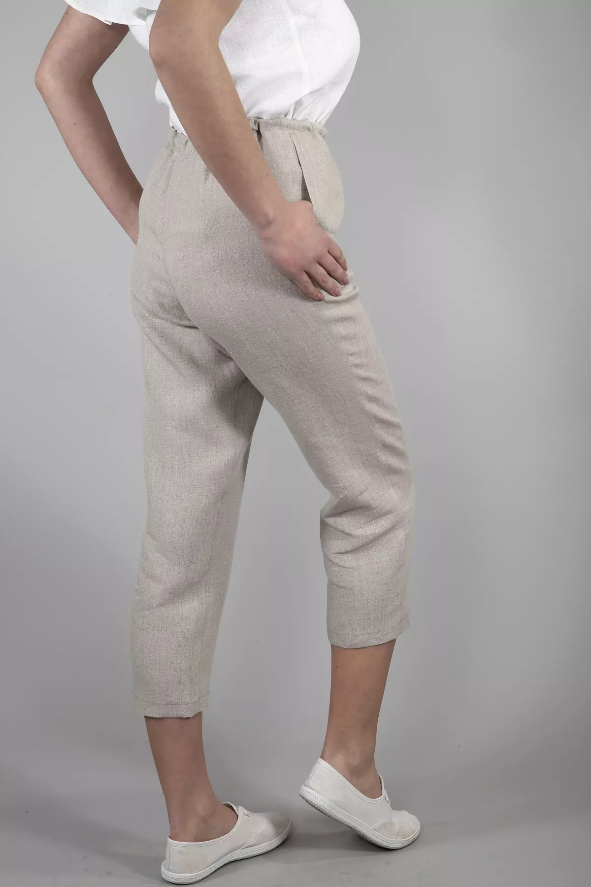 Ujęcie z boku i tyłu. Modelka stoi w lekkim rozkroku, trzymając dłoń w kieszeni. Widać, jak naturalny len miękko układa się na ciele. Nogawki są luźne, zapewniając komfort w ciepłe dni.