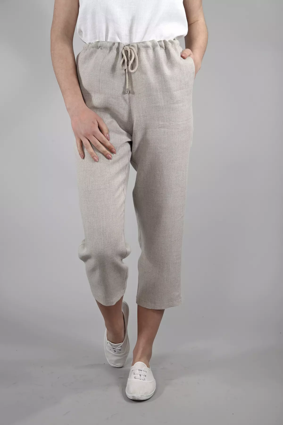 Modelka idzie w stronę obiektywu. Ma na sobie spodnie Mira w kolorze naturalnego lnu. Widać długość 7/8 (do połowy łydki) i swobodny krok. Stylizację uzupełnia biała, lniana bluzka i białe trampki.