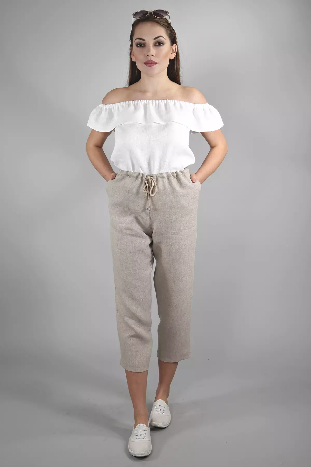 Modelka stoi prosto na szarym tle. Ma na sobie spodnie Mira w kolorze naturalnym i biały top. Ręce trzyma w kieszeniach bocznych. Spodnie wyglądają na bardzo wygodne i przewiewne.