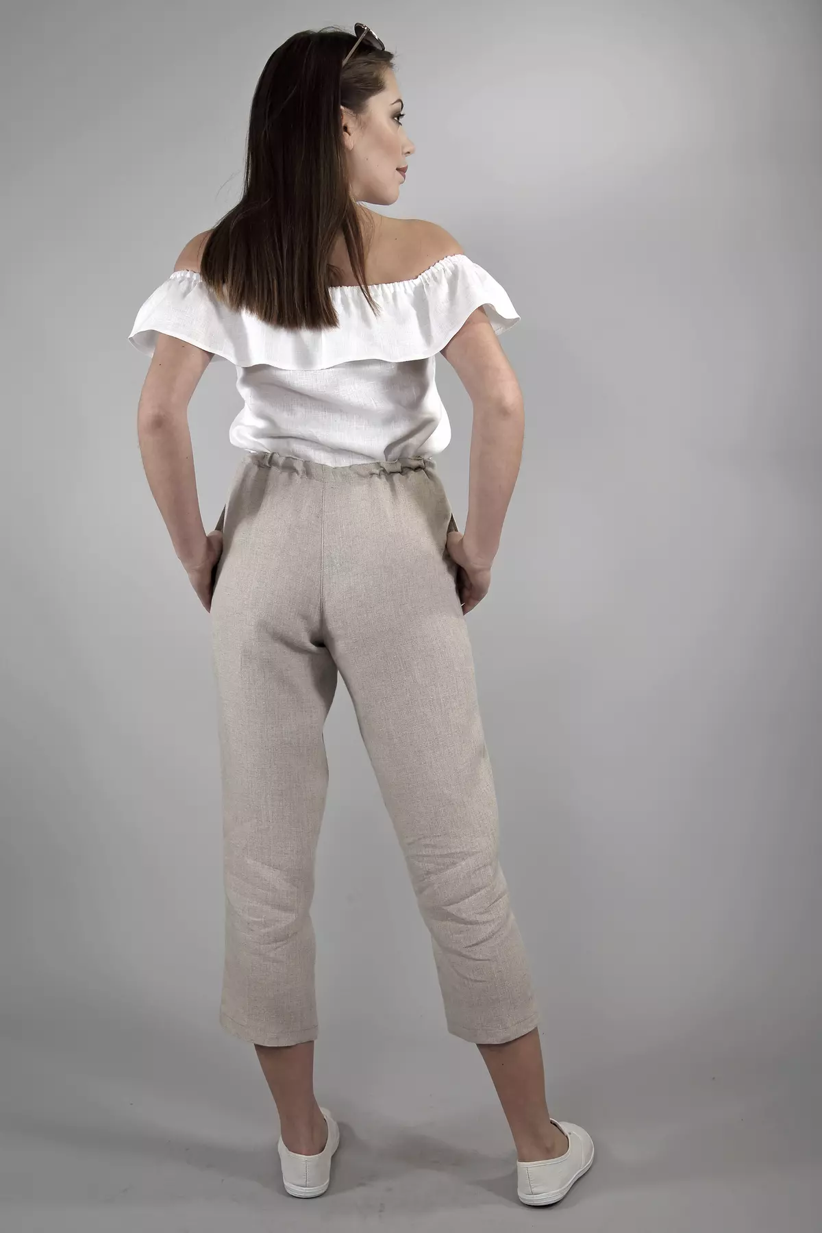 Widok sylwetki od tyłu. Spodnie Mira mają luźny krój w biodrach i proste nogawki kończące się w połowie łydki. Widać marszczenie w pasie spowodowane elastyczną gumką. Kolor tkaniny to piaskowy beż.