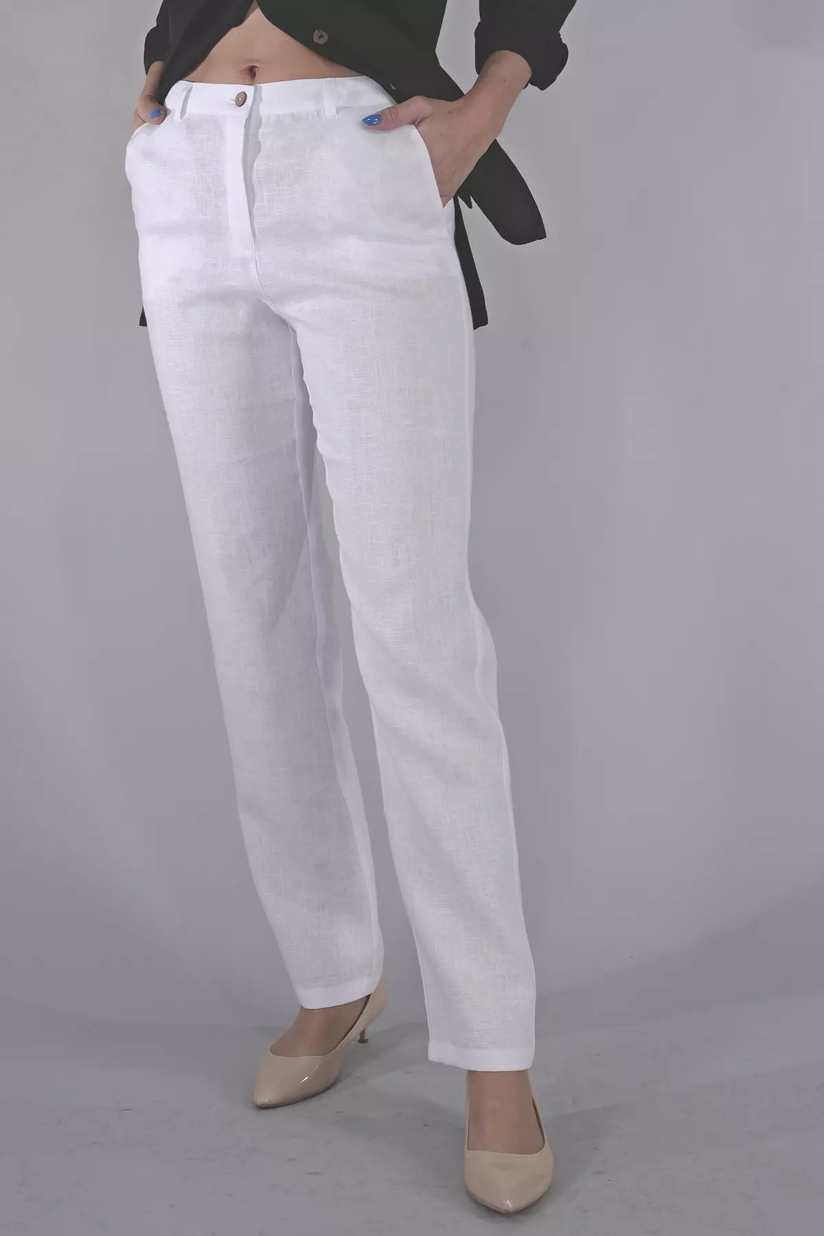 Zbliżenie na górną część spodni. Modelka trzyma dłonie w kieszeniach. Widać precyzyjne wykończenie paska, guzik w naturalnym kolorze oraz strukturę lnianej tkaniny.